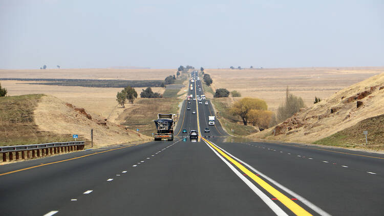 The N3 freeway from Johannesburg to Durban in South Africa, straight road to the horizon over dry landscape with cars and trucks from drivers point of view