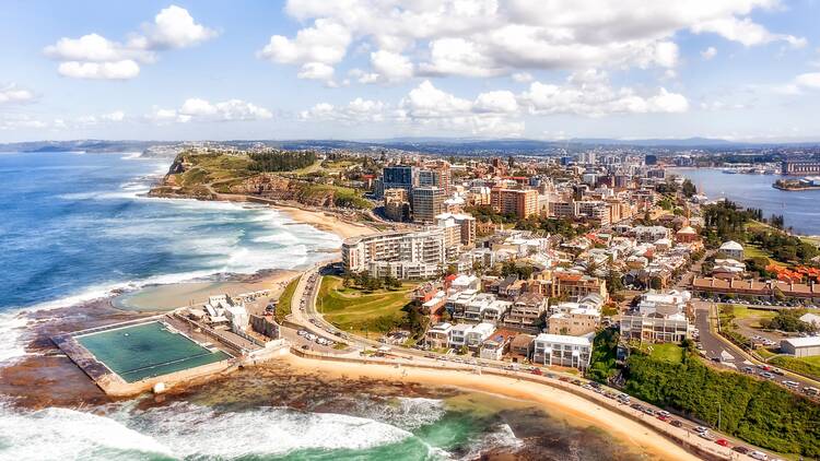 Panorama of Newcastle city on the hills over Hunter river and Pacific ocean with beaches, pool and surfers.