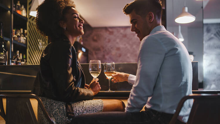 1921550834 Romantic couple on a date talking holding a glass of white wine sitting at the bar counter in the night - food and drink, people, lifestyle concept