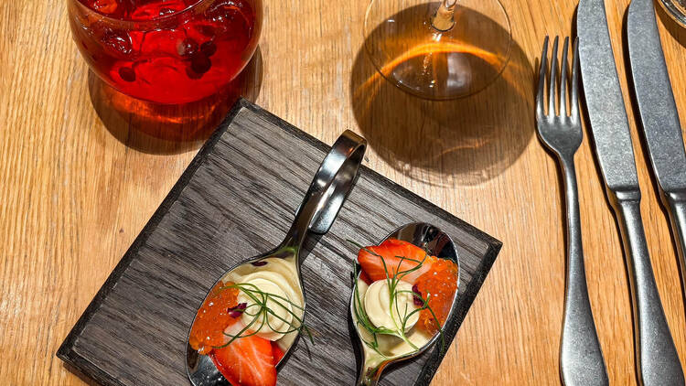 Lusikoilla tarjoiltu alkupala Tampereen Berthassa puupöydällä, vieressä juomalaseja ja aterimet.