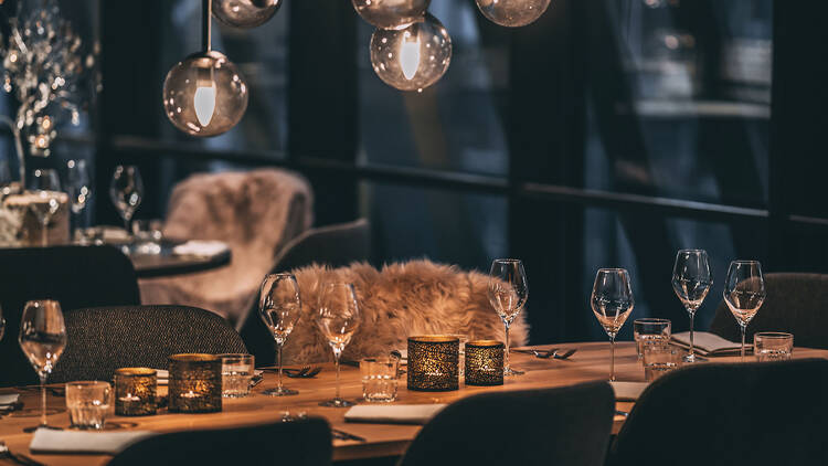 Illallispöytä Saivo Kitchen & Bar of Momentsissa Tampereella, katetut pöydät, viinilasit ja hämärä valaistus ravintolasalissa.