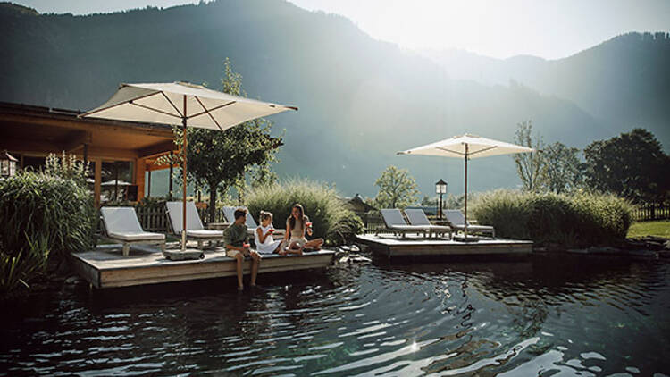A family sit on decking next to Familien Natur Resort Moar Gut's swimming lake