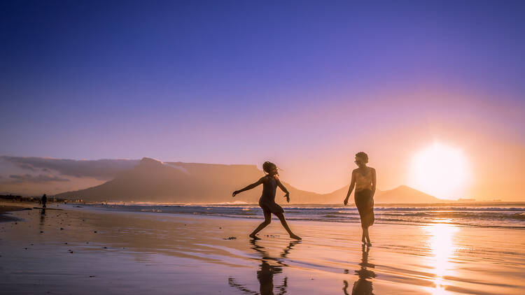Two women dancing on the beach at sunset, with Table Mountain and Cape Town in the background, Milnerton Beach, Cape Town, South Africa