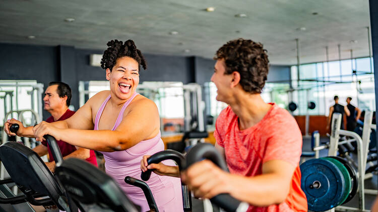 Friends talking while exercising on elliptical cross trainer at gym