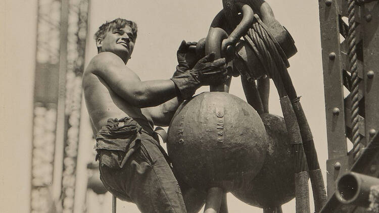 Sepia image of a construction worker hanging off a large steel ball in mid-air