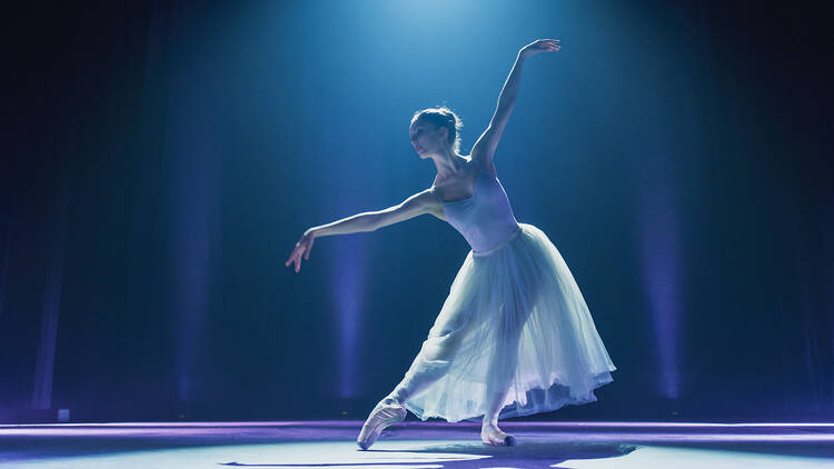 1560332447 Cinematic Shot of Ballerina in Pointe Shoes and White Tutu Dancing and Rehearsing on Classic Theatre Stage with Dramatic Lighting. Graceful Classical Ballet Female Dancer Performing a Choreography