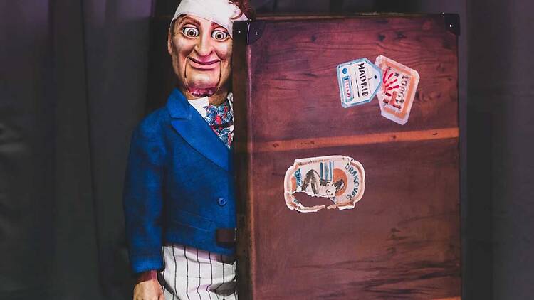 A puppet stands behind a wood partition. 