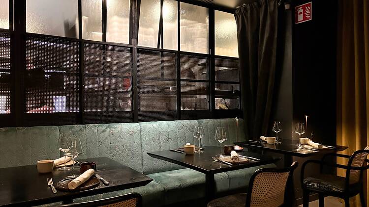 Moderni fine dining -ravintola, jossa on tunnelmallinen valaistus, tyylikkäät mustat pöydät ja mintunvihreä samettisohva. Moderni fine dining -ravintola, jossa on tunnelmallinen valaistus, tyylikkäät mustat pöydät ja mintunvihreä samettisohva.