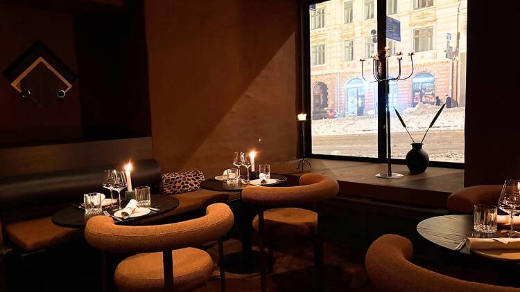 Tunnelmallinen ravintolalounge, jossa lämpimät ruskeat sävyt, kynttilävalaistus ja suuret ikkunat luovat kutsuvan fine dining -ilmapiirin Tunnelmallinen ravintolalounge, jossa lämpimät ruskeat sävyt, kynttilävalaistus ja suuret ikkunat luovat kutsuvan fine dining -ilmapiirin