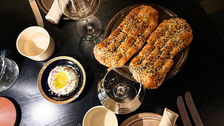 Tummaa pöytää vasten aseteltu annos tuoretta seesaminsiemenillä viimeisteltyä leipää ja mausteista levitettä luo houkuttelevan fine dining -ruokapöydän. Tummaa pöytää vasten aseteltu annos tuoretta seesaminsiemenillä viimeisteltyä leipää ja mausteista levitettä luo houkuttelevan fine dining -ruokapöydän.