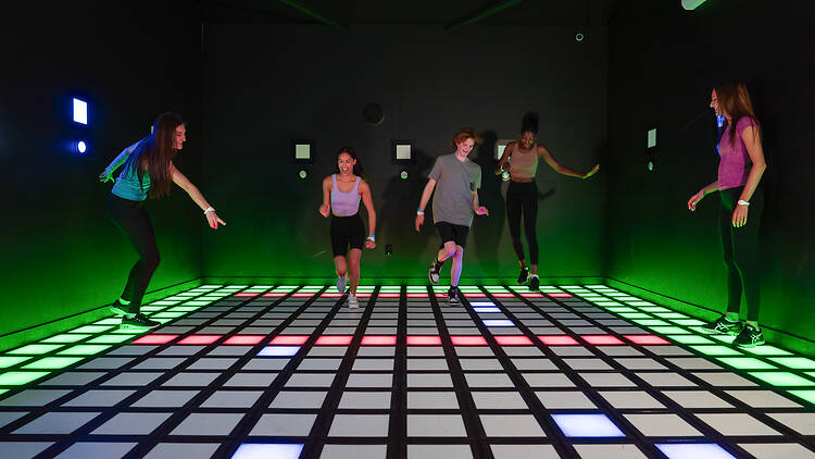 Ihmiset pelaavat vilkkuvien valojen lattialla elämyspeliä Activate Gamesin Helsingin toimipisteessä