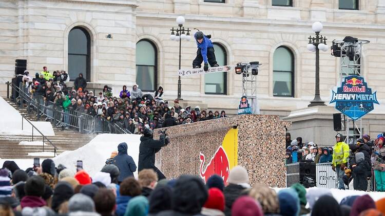 Lumilautailija hyppää ilmaan Suomen pankin edustalla, yleisön edessä Helsingissä