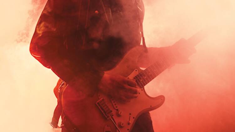 A promotional image of a guitarist surrounded by a red and orange fog.