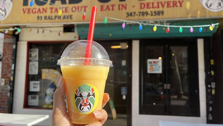 A hand holding an orange smoothie outside of the Toad Style restaurant