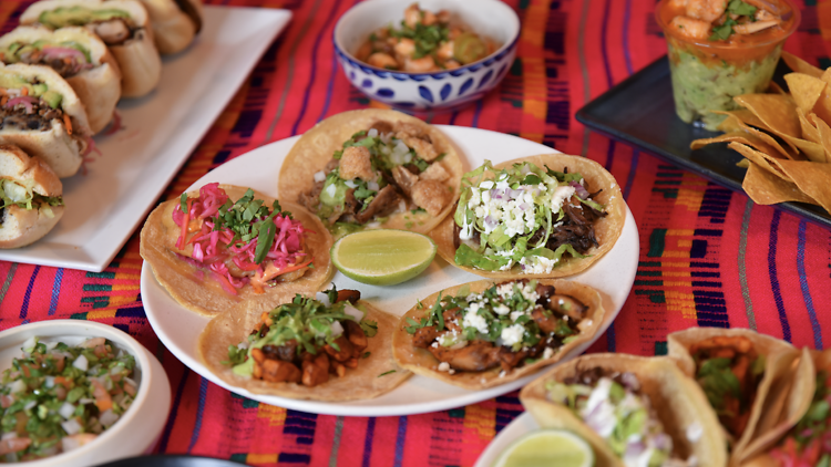 Tacos Fonda table spread of tacos, guacomole, salsas on a vibrant stripped table cloth. 
