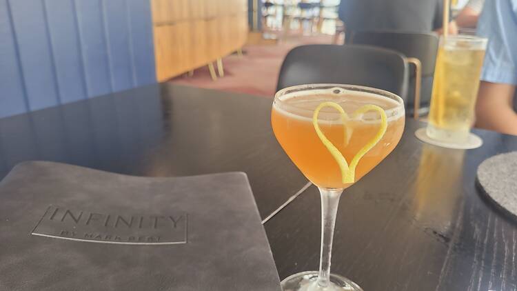 A cocktail with a yellow love heart made from lemon rind