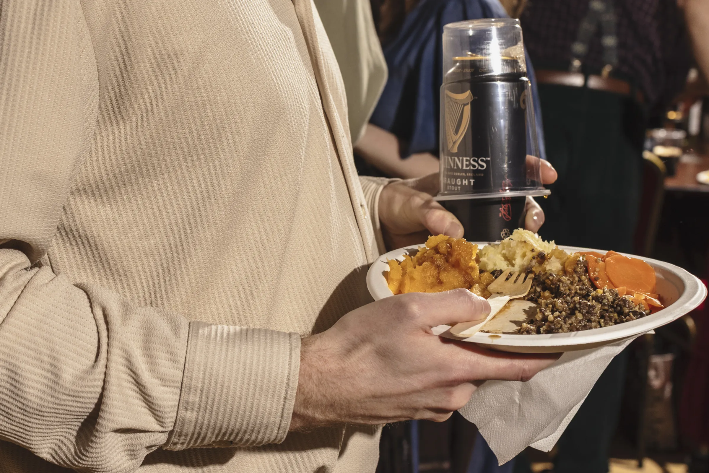 Person holding a can of Guinness and a paper plate with haggis, neeps and tatties 