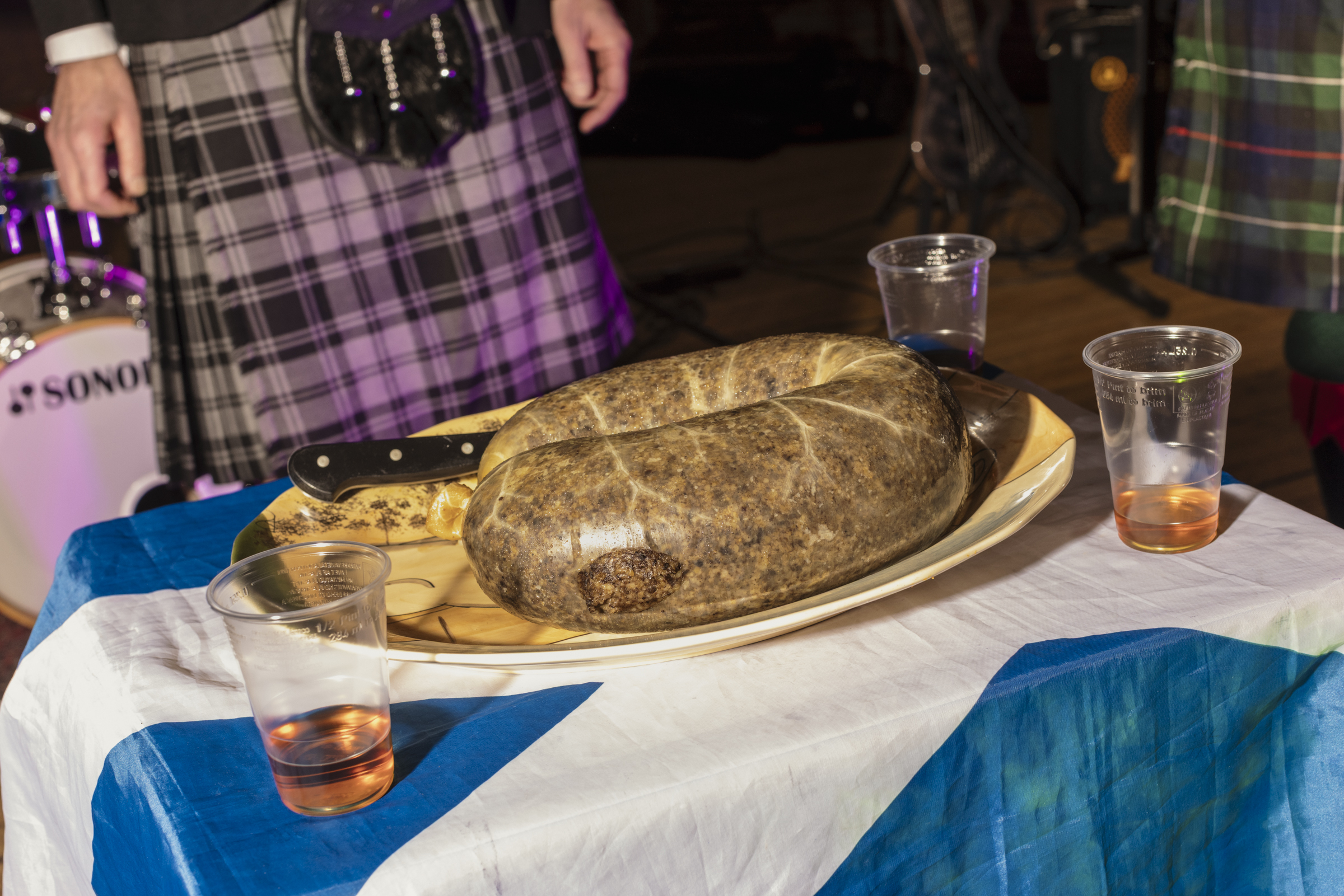 Big haggis on a table covered with a Scottish flag with cups of Irn Bru 