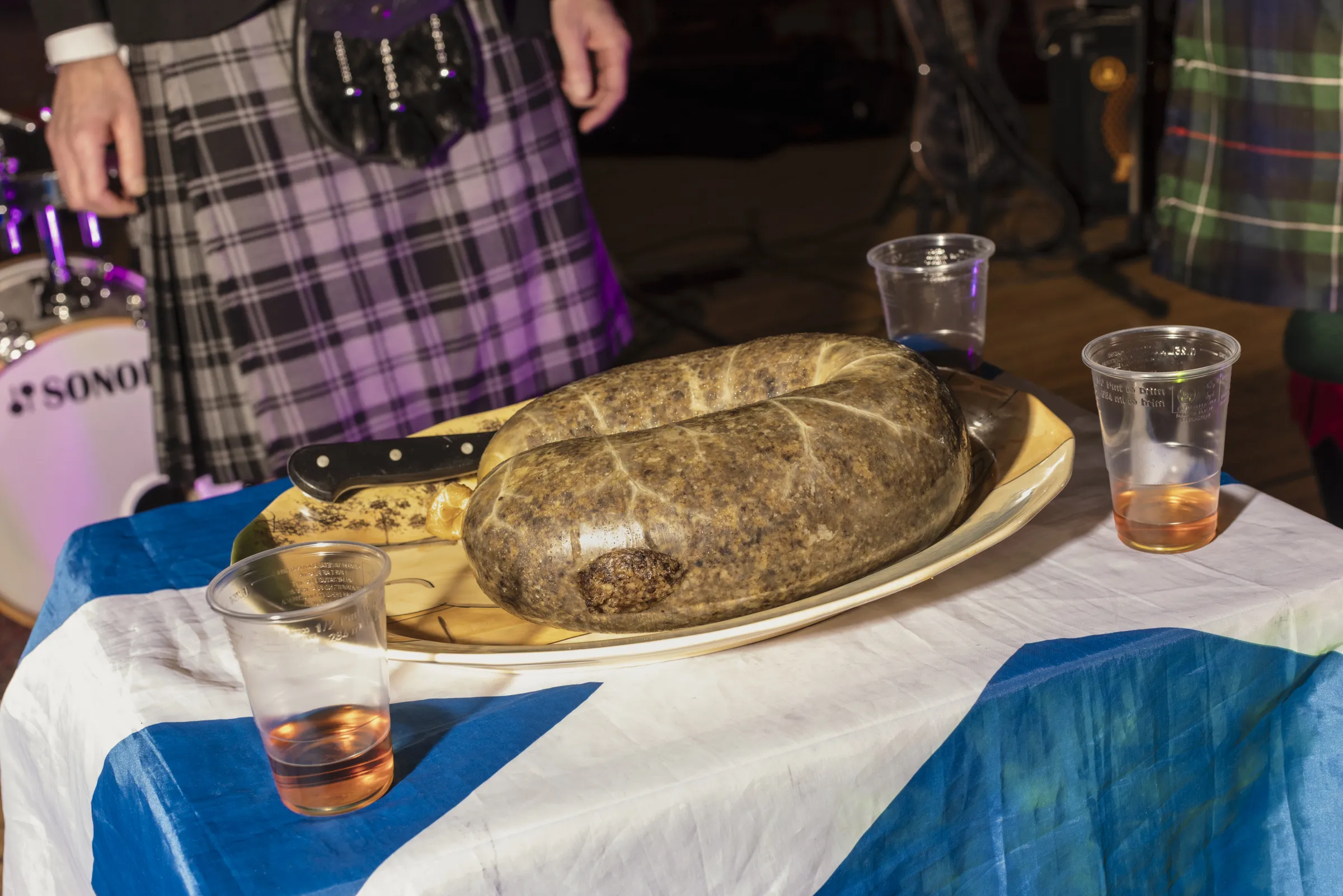 Big haggis on a table covered with a Scottish flag with cups of Irn Bru 