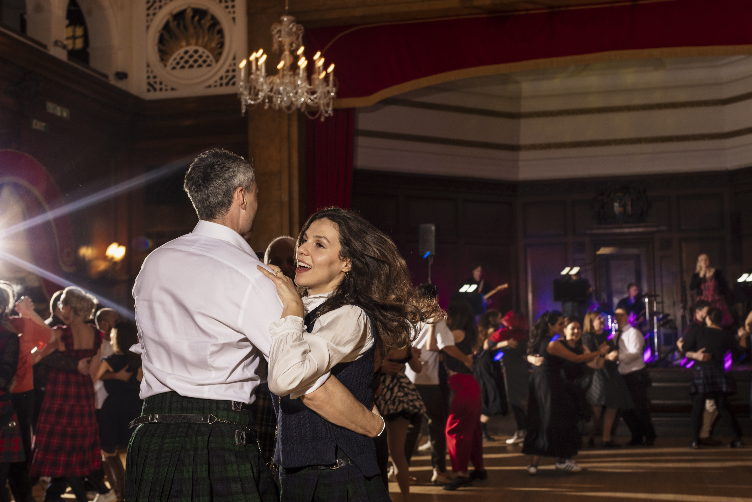 People dancing in a big hall with high ceilings and chandeliers 