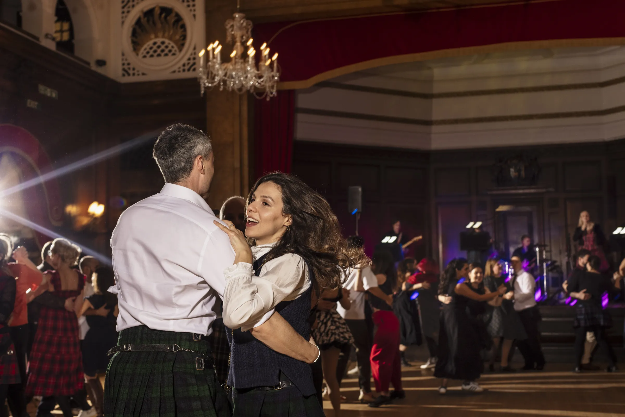 People dancing in a big hall with high ceilings and chandeliers 