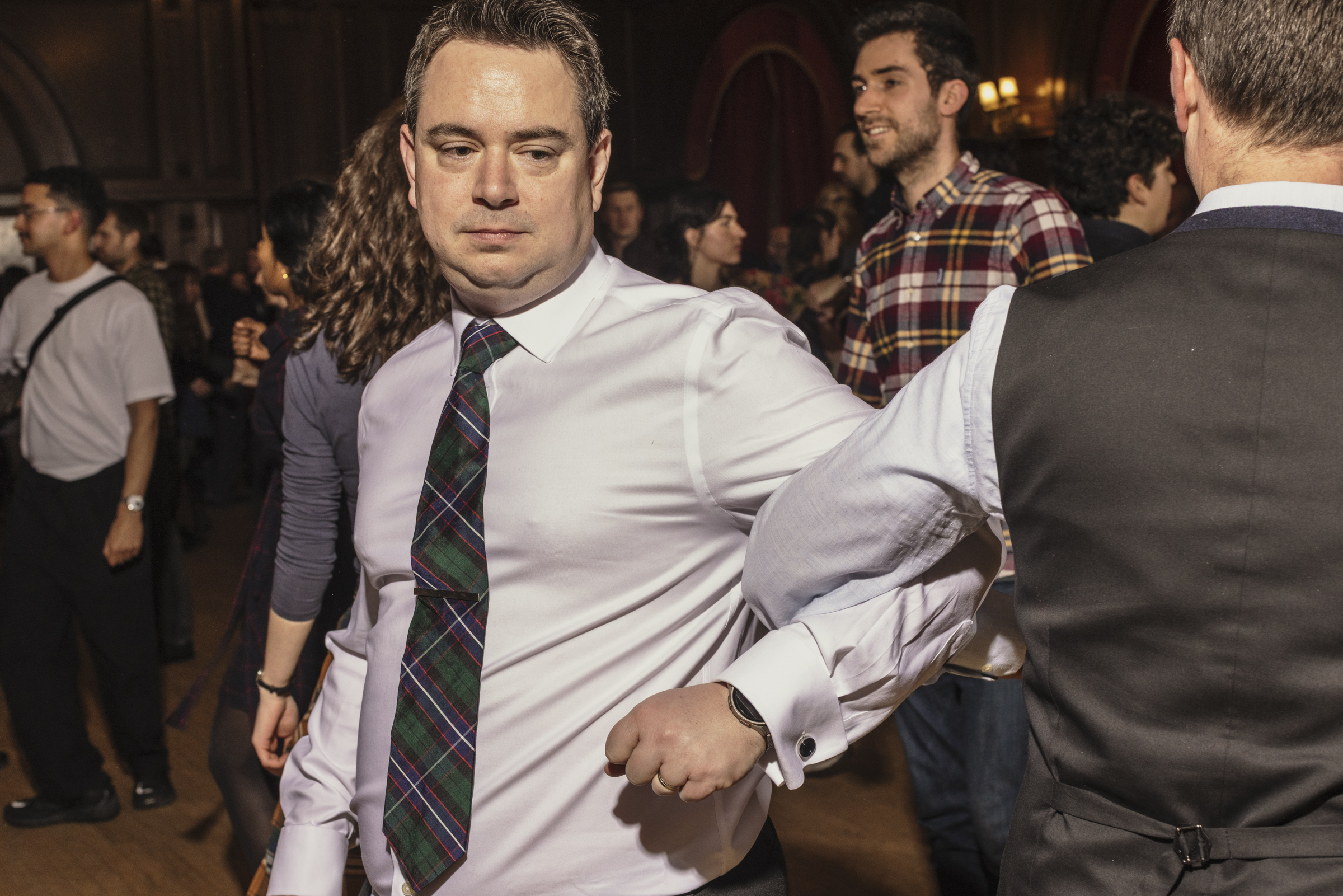 Two men in tartan ties linking arms during a dance 
