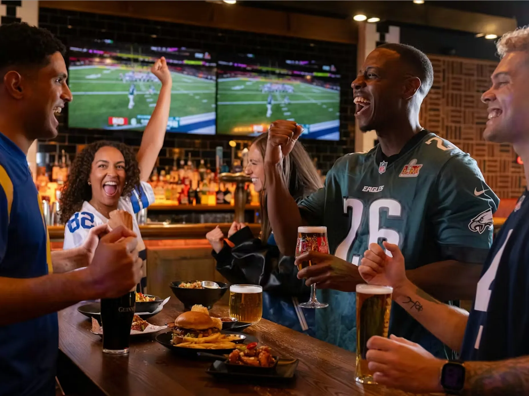 Three men and two women wearing NFL jerseys watch a game at Box Piccadilly