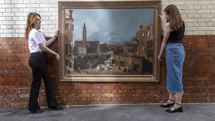 Two women hold up a life-sized recreation of a farmyard painting