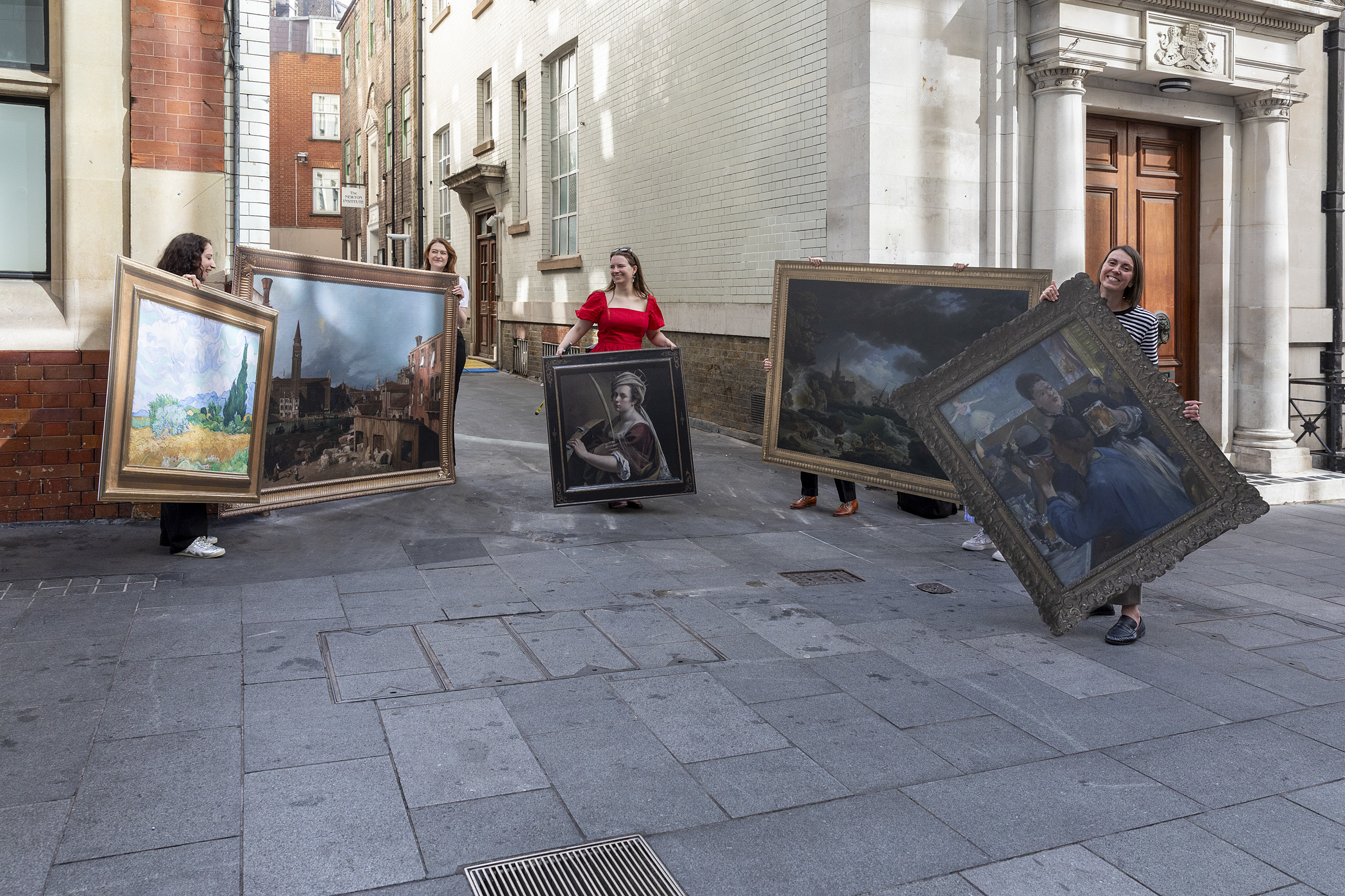 Five people carry life-sized recreations of famous artworks through a sunny London street