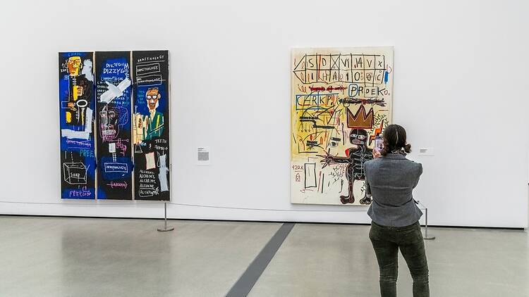 People looking at Basquiat paintings in an art gallery