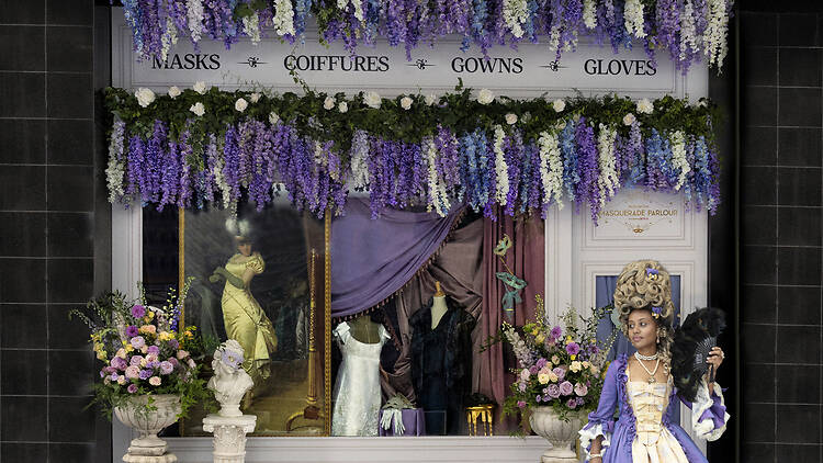 A person in Regency-era costume stands out the front of a dress shop.