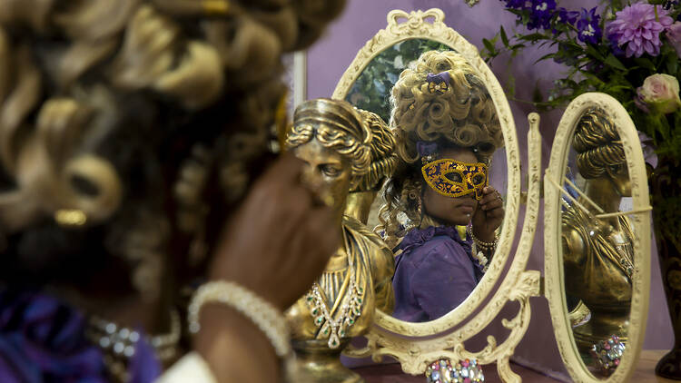 A person in a masquerade mask looking into a mirror.
