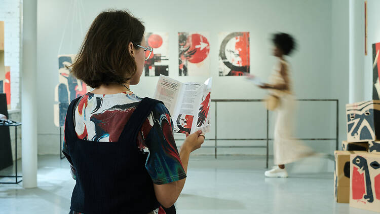 Young woman with dark straight hair looking through information about exhibition events in brochure in gallery hall
