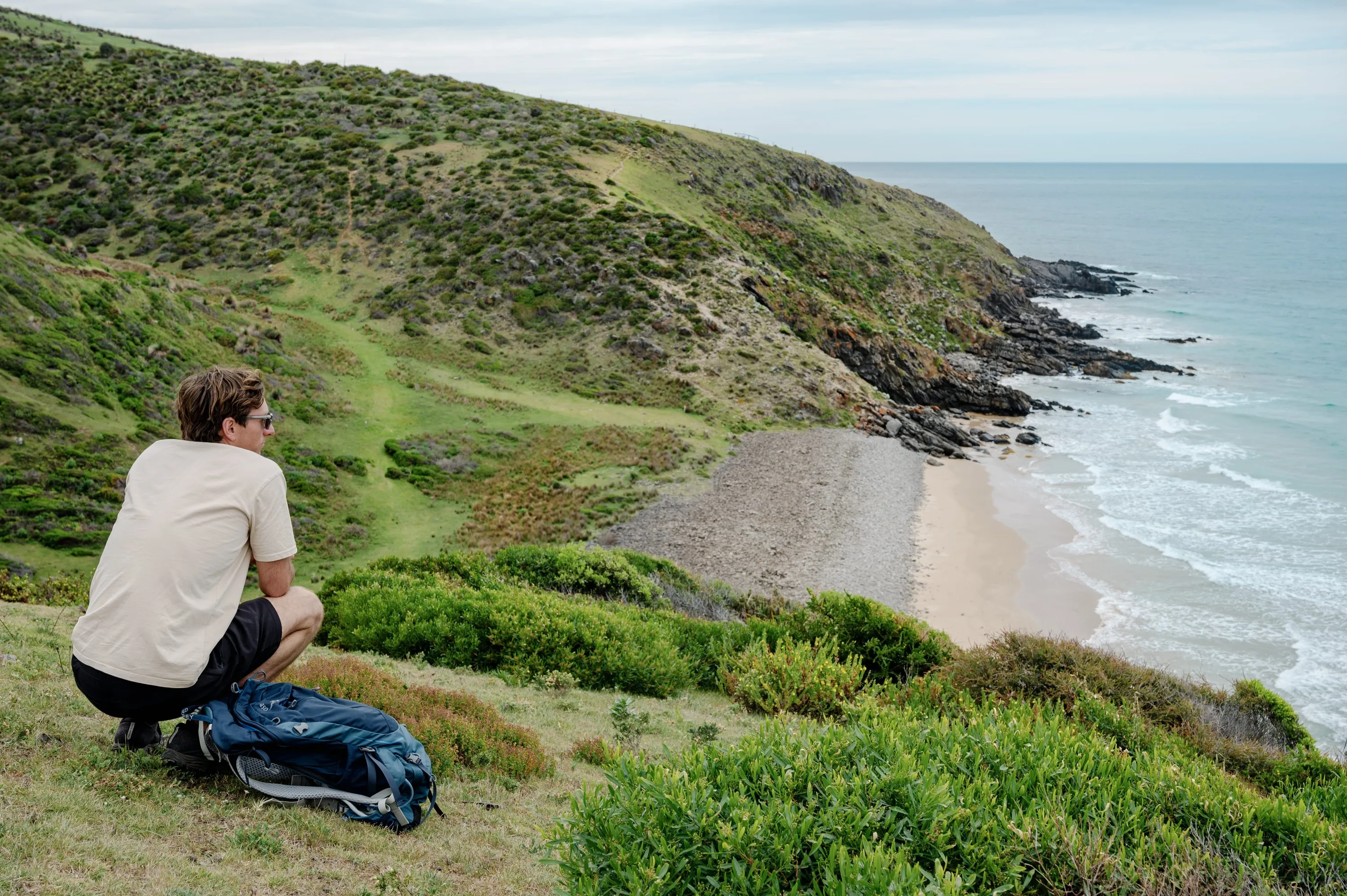 Man squatting on hill looking at beach