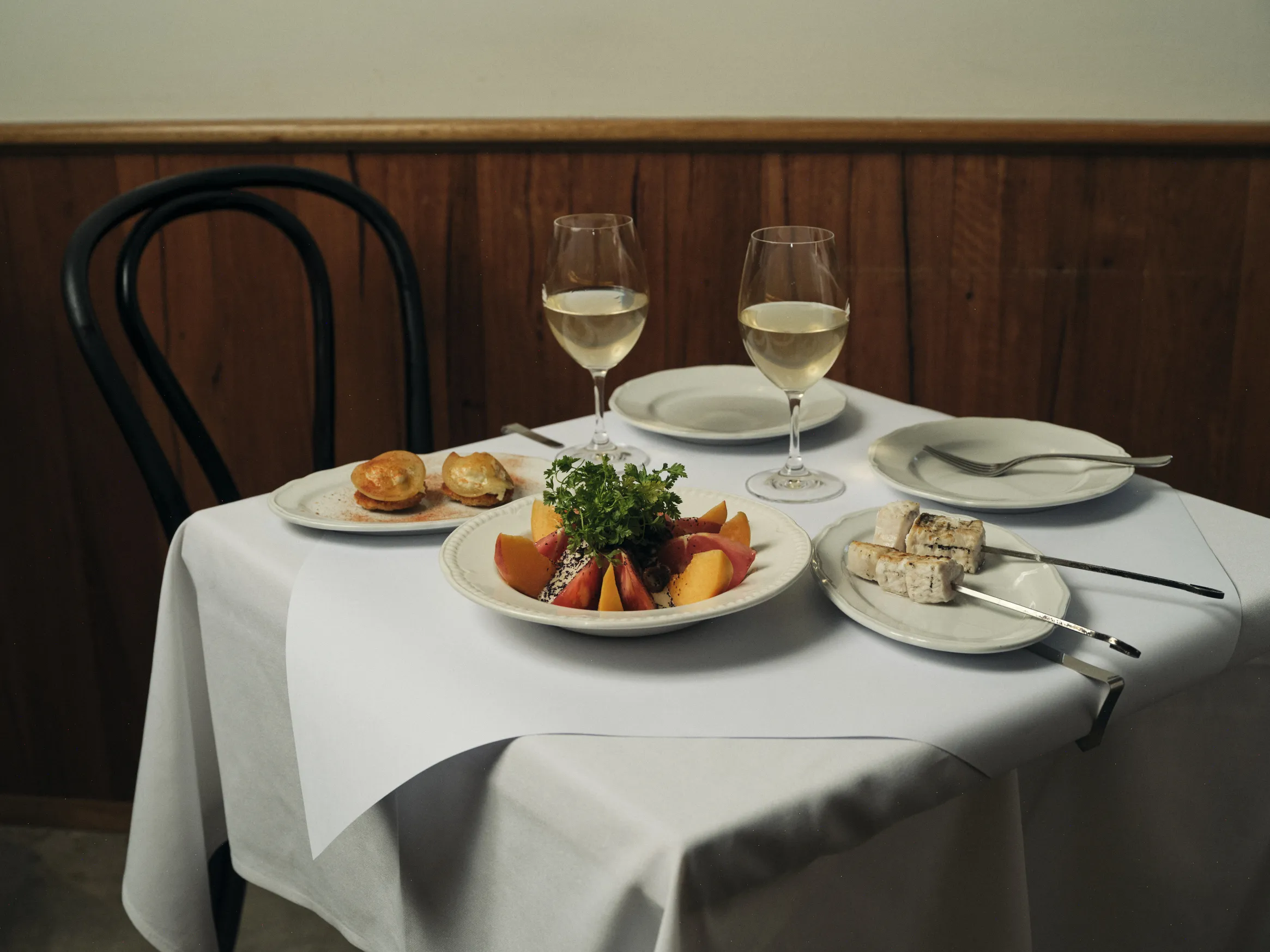 A table laden with food and two glasses of white wine.