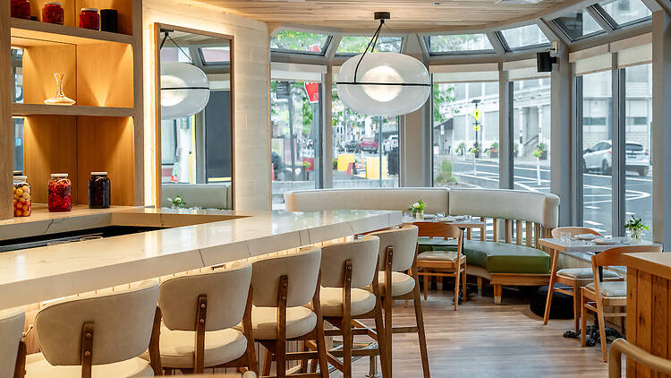 Interior of Fallow Kin in Cambridge showing bar seating, light wood finishes, curved banquettes and large globe pendant lights by the windows.