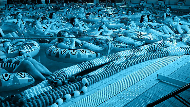 Suuri joukko ihmisiä kelluu uimarengailla uima-altaassa katsomassa elokuvaa