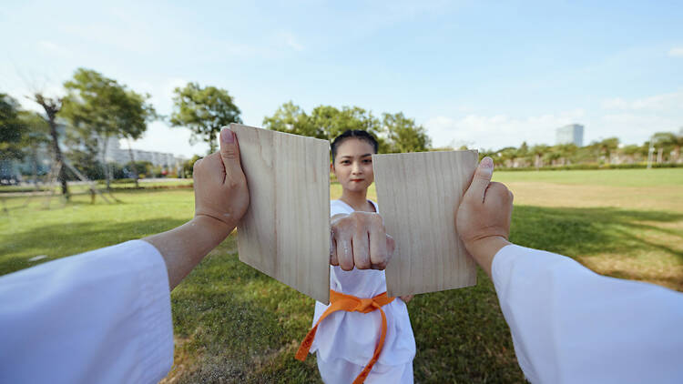 2050216264 Taekwondo sportswoman breaking wooden board with her fist
