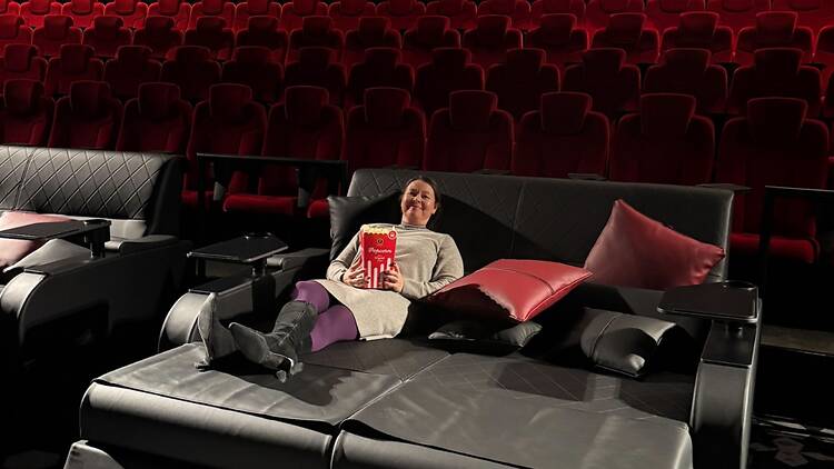 Nainen makaa popcornkulhon kanssa leffateatterin istuimella, joka on levitetty sängyksi