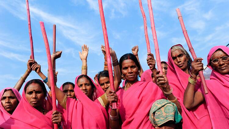 Women in pink saris raising pink sticks.