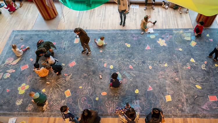 Aerial shot of several children drawing on a giant chalkboard at Imagine Children’s Festival