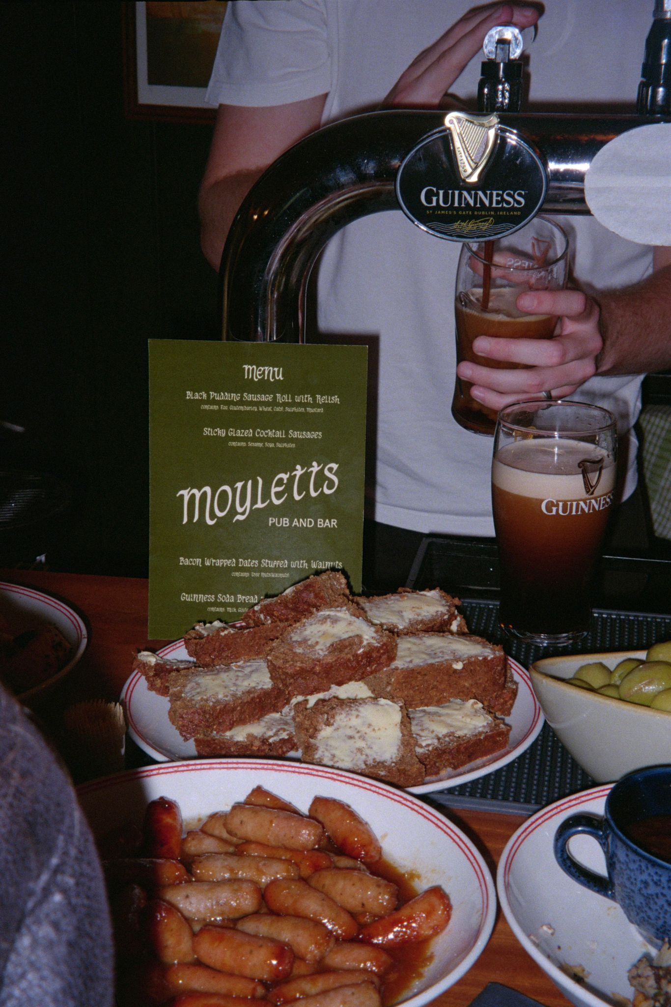 Barkeep pouring a pint of Guinness behind plates of food at the bar