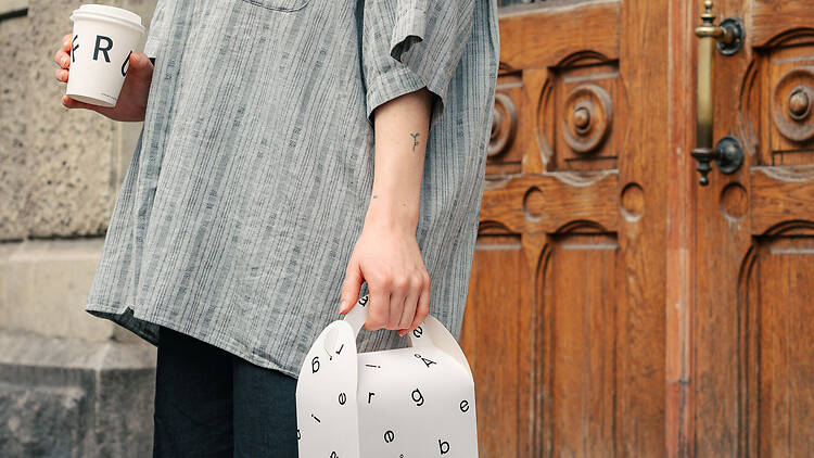 Asiakas pitelee Bageri Å:n leivosrasiaa ja Fruktin take away -kahvia puuoven edessä Turussa.