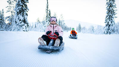 A woman speeds down a snowy hill on a sled. A woman speeds down a snowy hill on a sled.