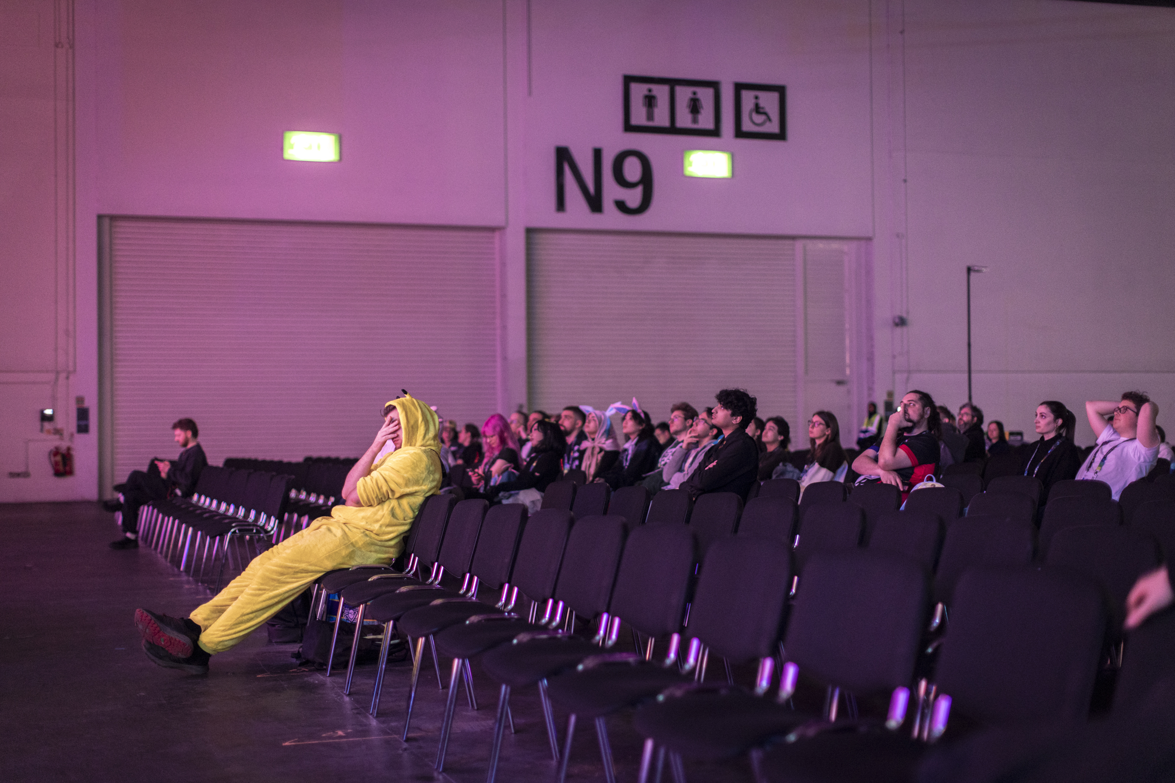 Man in Pikachu costume sat alone in a long row of chairs with hand over face