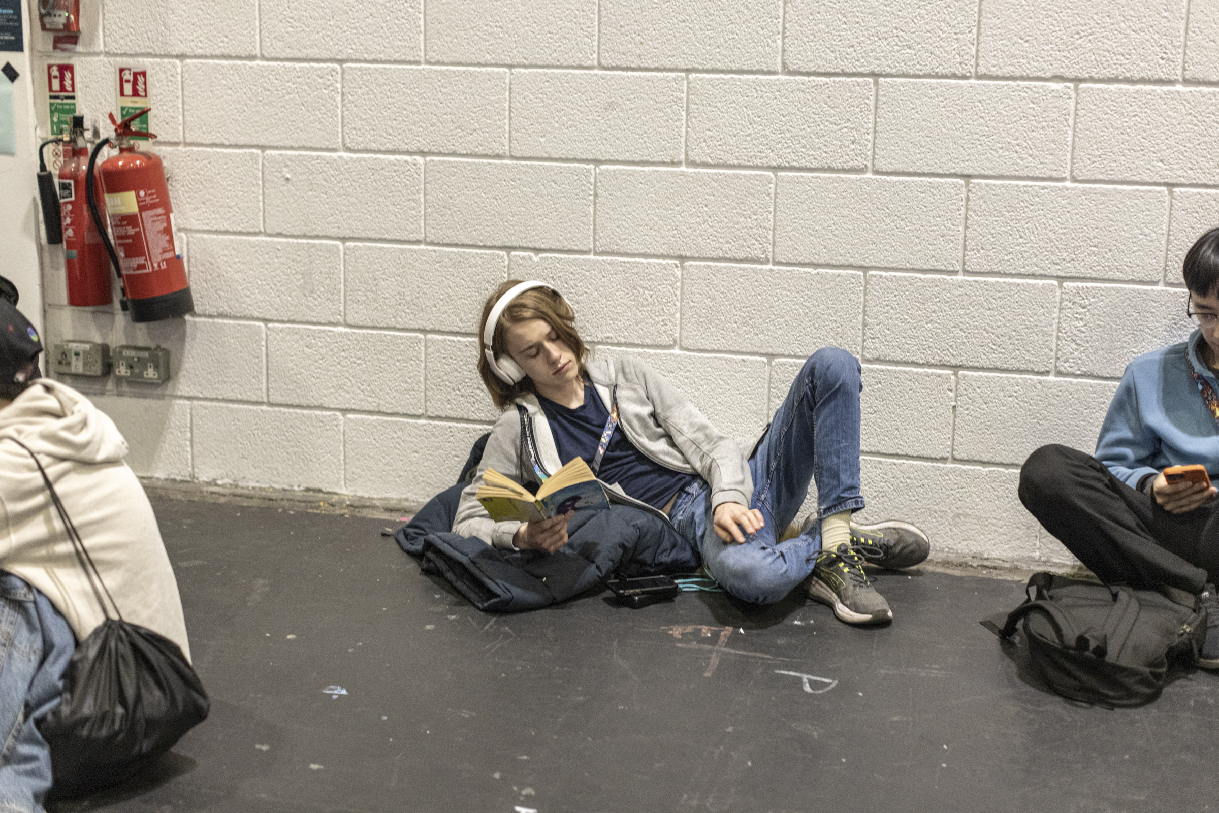 Person sat on the floor reading a book with headphones on