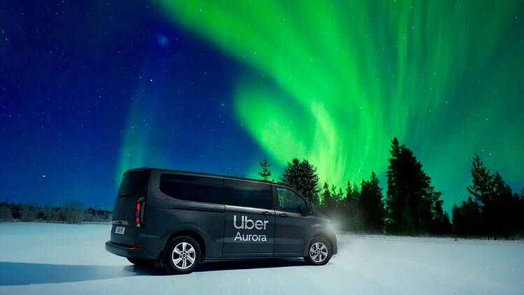 Kuvassa näkyy Uber Aurora ‑brändätty auto seisomassa lumisella maisemalla kirkkaiden vihreiden revontulien loistaessa taivaalla. Kuvassa näkyy Uber Aurora ‑brändätty auto seisomassa lumisella maisemalla kirkkaiden vihreiden revontulien loistaessa taivaalla.