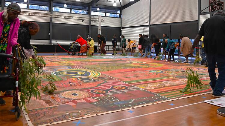 Ngurrara artists, family members and guests circling the canvas at Ngurrara Canvas II honouring ceremony Broome 2025