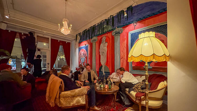 Hi-Hat-baarin seinää koristaa punasininen seinämaalaus, miehiä istuu nojatuoleilla