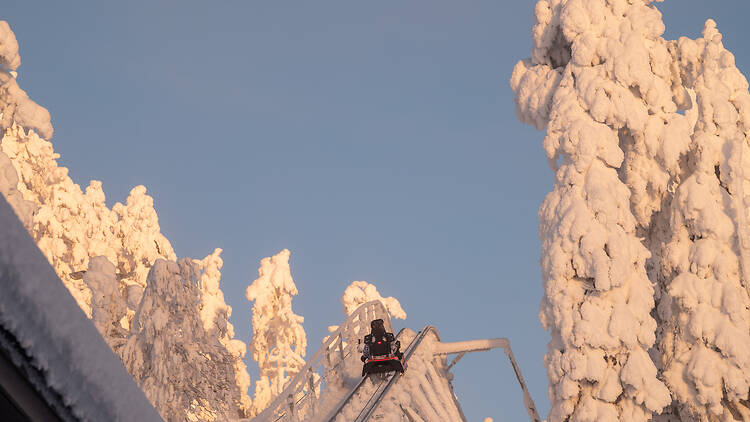 Kelkka nousee ylös pitkin Ruka Coaster vuoristoradalla vierellään lumisia puita Kelkka nousee ylös pitkin Ruka Coaster vuoristoradalla vierellään lumisia puita